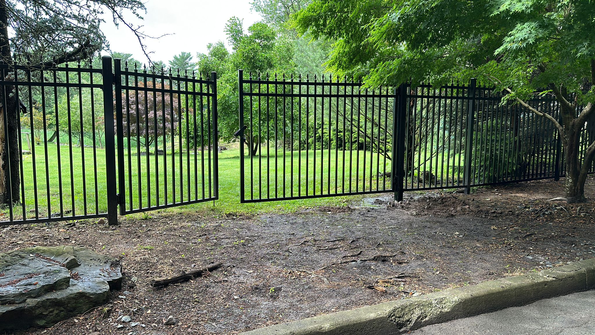 Black ornamental iron fence with spear finials bordering a landscaped lawn