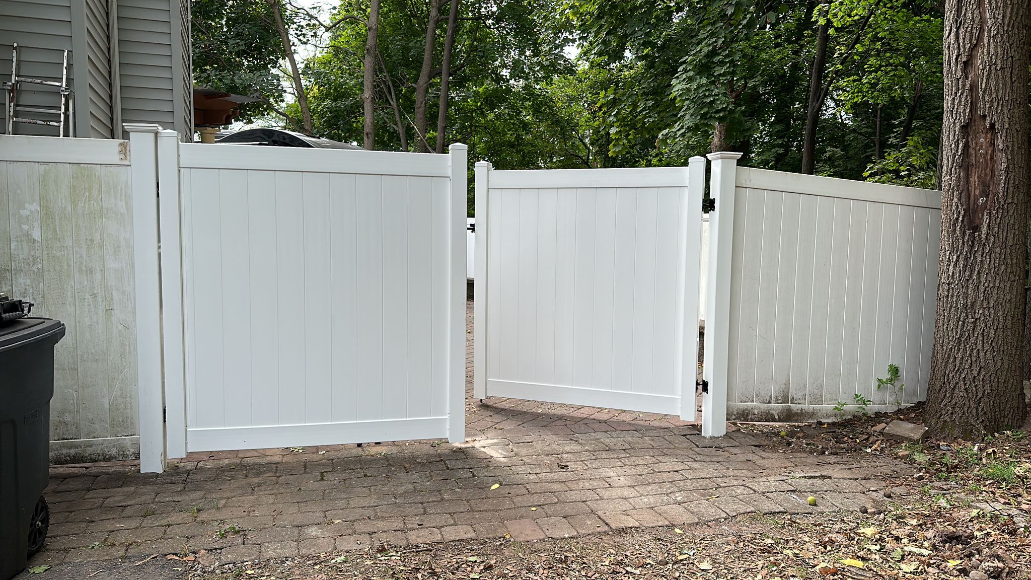 White PVC double gate opening onto a paver driveway