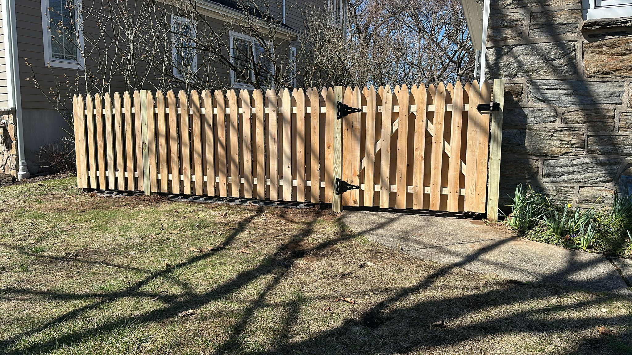 Scalloped wood picket fence with matching gate beside a stone house