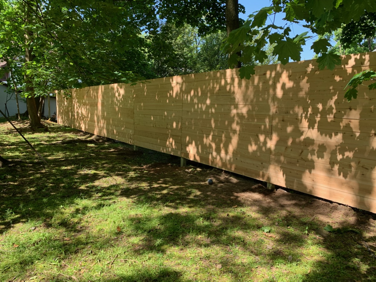 Horizontal cedar wood privacy fence installed along a shaded backyard